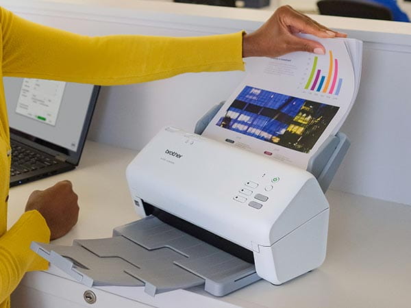 Woman in office putting large stack of full color double-sided documents in scanner's automatic document feed