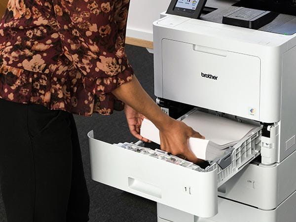 Woman adding ream of paper to printer's paper tray