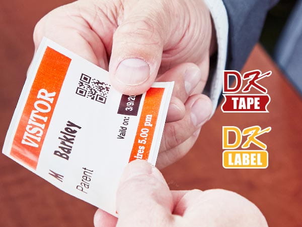 School administrator handing red and black on white visitor badge with QR code to visiting parent, with DK Label and DK Tape logos
