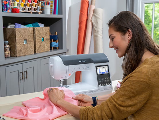 Woman sitting at table sewing pink fabric on a Brother sewing machine