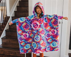 Woman wearing a tie dye fleece hooded blanket and standing next to staircase in home.