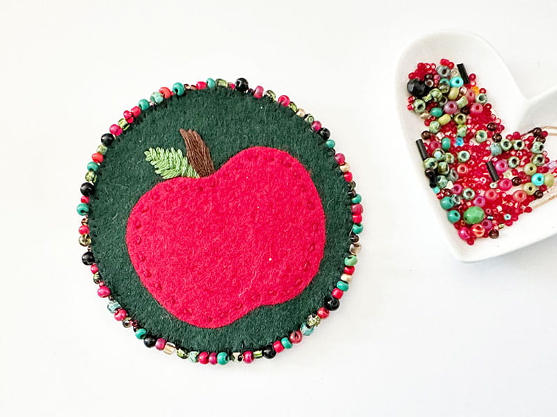 Felt apple pin next to heart dish containing beads