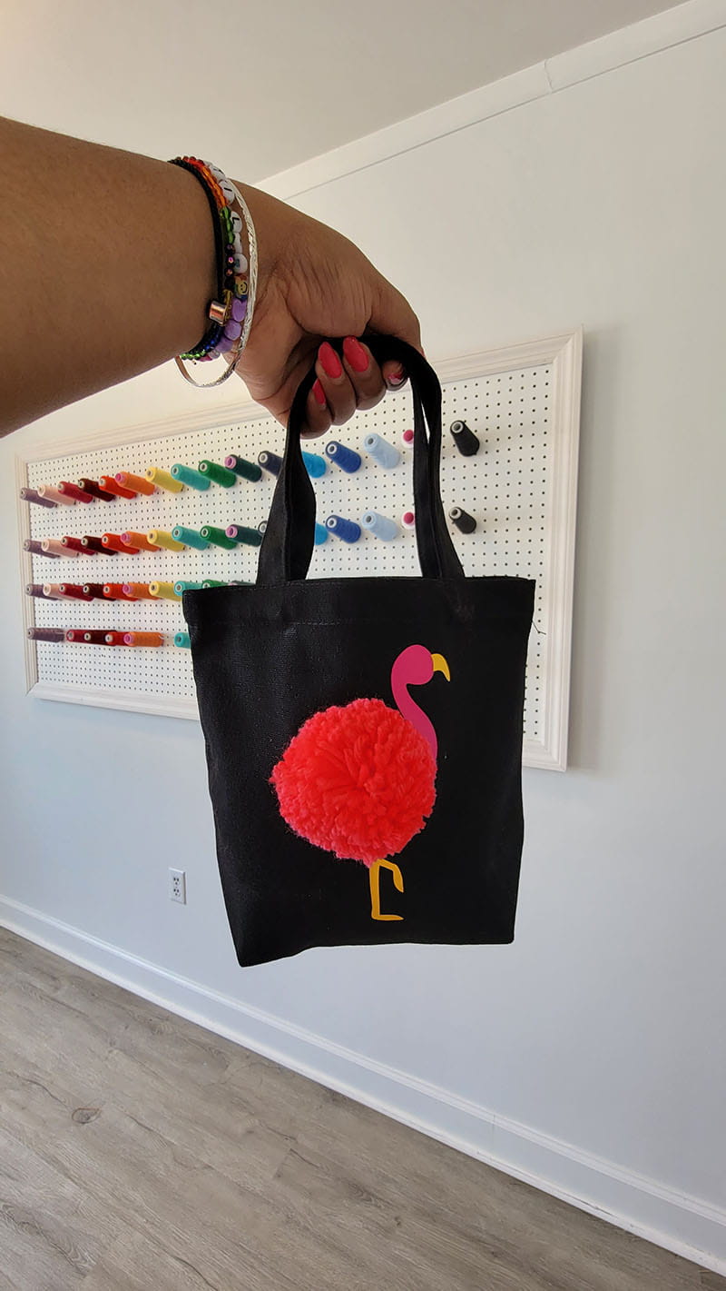 Woman holding completed flamingo tote in front a colorful wall display. 