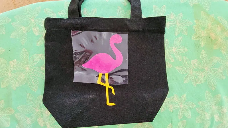 Full flamingo body on a black tote laid out on ironing board.