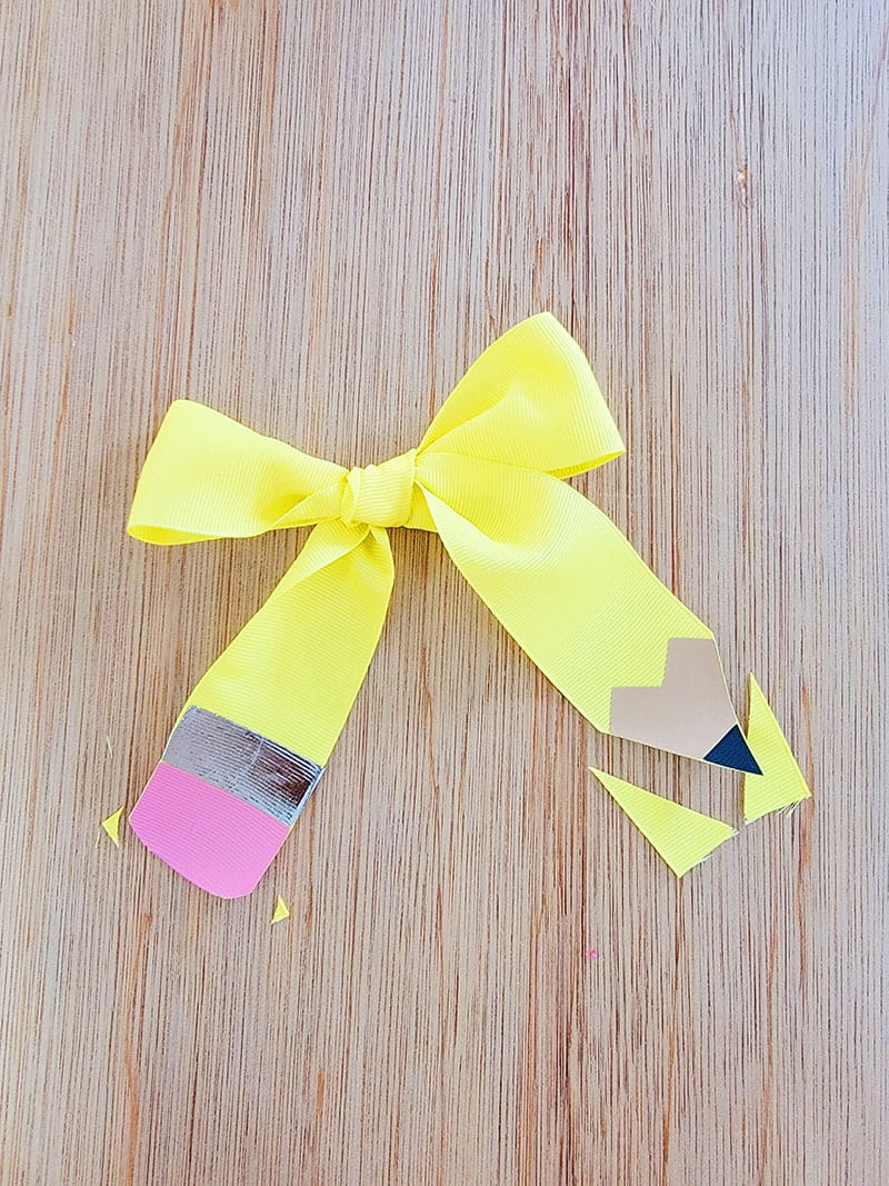 Yellow bow made to look like a pencil on a wood background