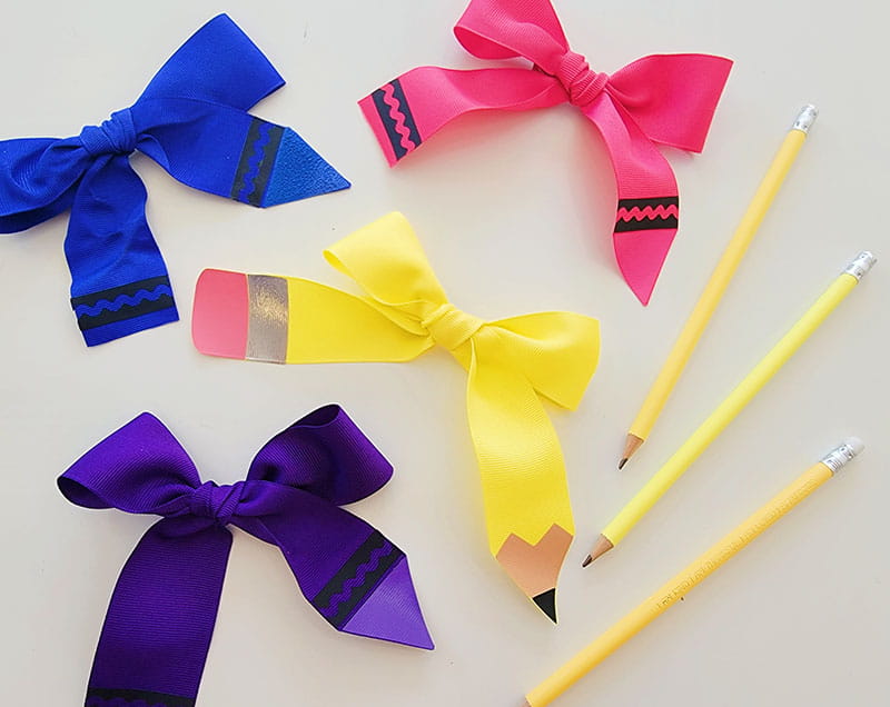 Finished pencil and crayon hair bows next to pencils on a gray background