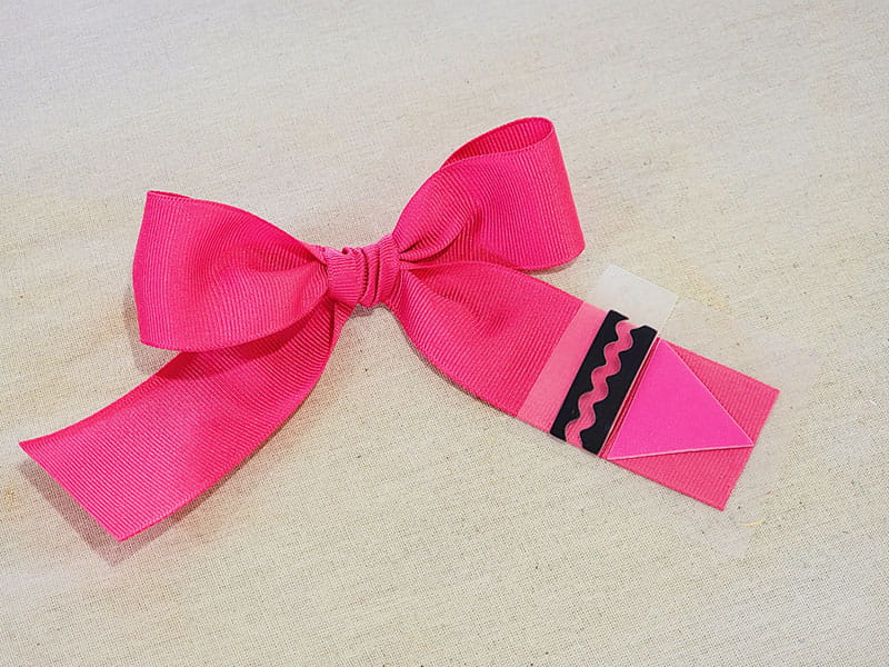 Pink bow fashioned to look like a crayon with crayon tip overlaid.