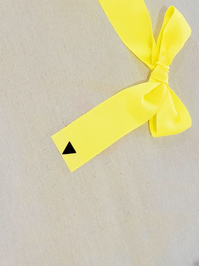 Yellow hair bow made to look like pencil with a black pointed tip on right side 