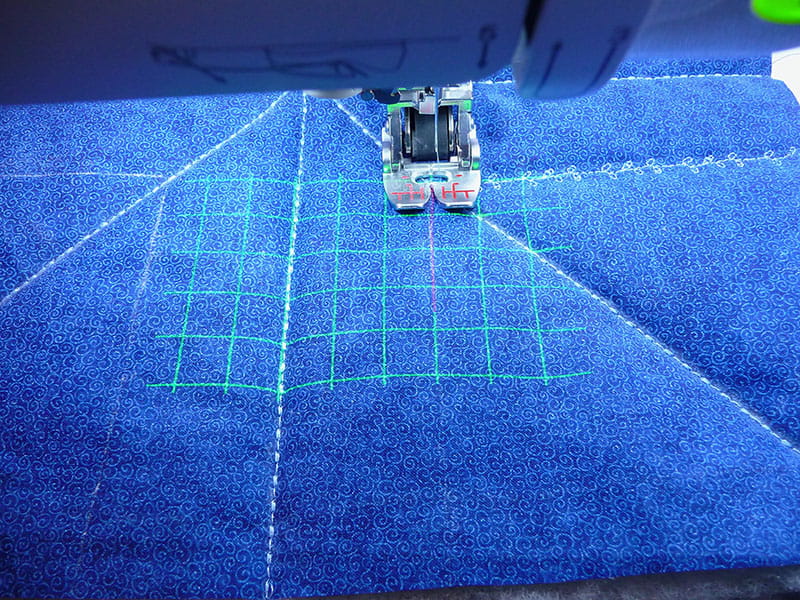 Brother Sewing machine with lasers on the blue fabric displaying the area that will be sewn