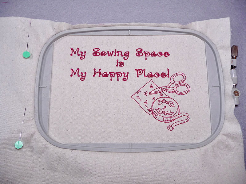 My Sewing Space is My happy place embroidered on fabric in pink with visible embroidery hoop