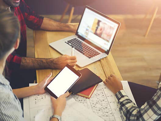 Three co-workers gathered around an Apple laptop