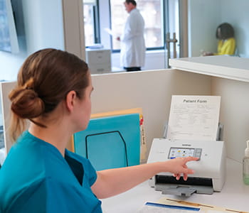 Healthcare worker loading document into a Brother scanner
