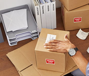 Person affixing a label created with QL-1100C label printer to a box on a desk. 
