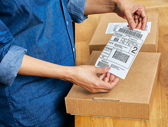 Close up of person placing a shipping label printed with the QL-1100c label printer on a brown box. 