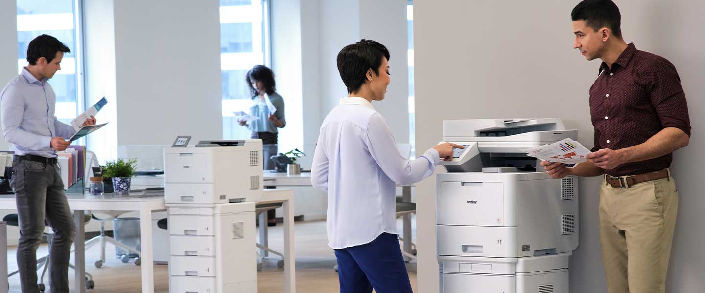 People in a large office talking near the printers featuring the Brother MFC-L9670CDN and HL-L9470CDN