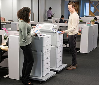 Co-workers using Brother Workhorse series printers near desks. Models shown: HL-L9470 and MFC-L9670