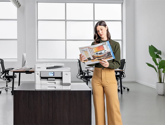 Woman in an office setting next to the Brother MFCJ6975 business inkjet printer.