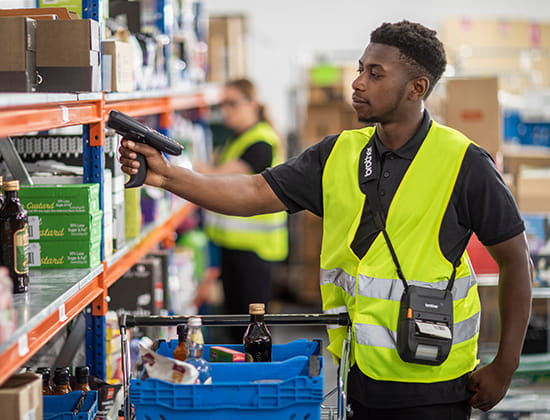 Man in yellow utility vest using a Brother Rugged Jet to scan item on shelf. 