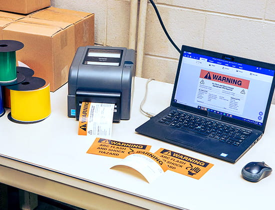 Brother Label printer creating safety signage on a desk next to a laptop.