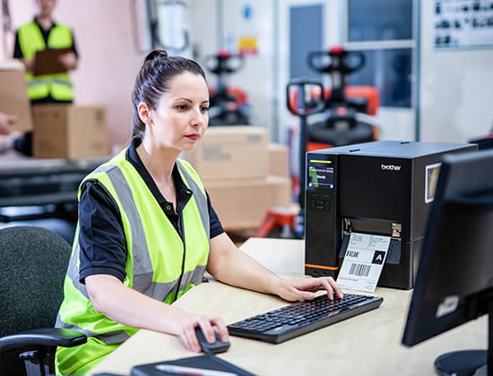 Woman in utility vest on a desktop computer creating labels to be printed on Brother Titan Industrial label printer.