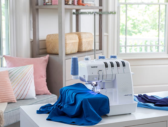 Side angle of Airflow 3000 serger in a brightly lit, white living room with blue garment in work area