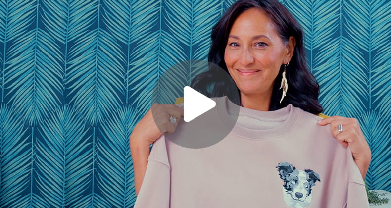 Video play button overlaid on image of woman holding a sweatshirt embroidered with Stellaire2 embroidery machine.