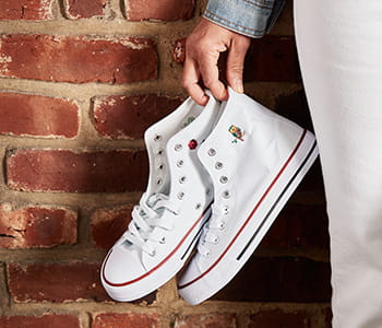 Person holding high-top sneakers against a brick wall. Sneakers feature an embroidery patter from iBroidery.