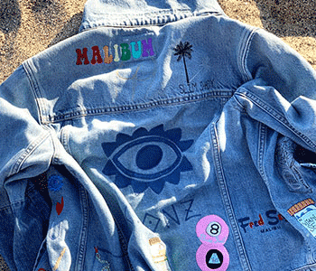 Embroidered denim jacket on sand with palm tree design and 'Malibum' text