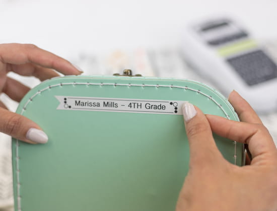 Person putting label with "Marissa Mills - 4th Grade" on a pencil case.