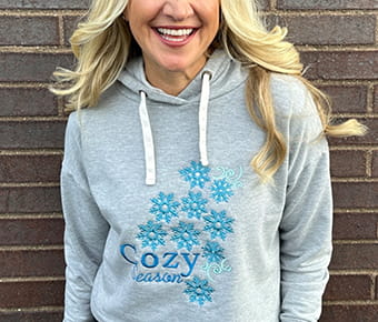 Woman wearing a gray sweatshirt with blue snowflake embroidery