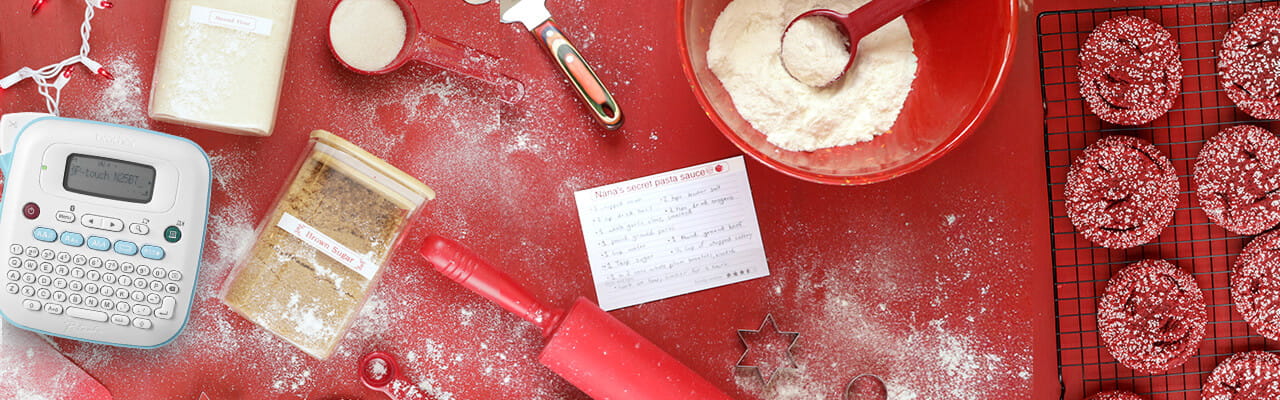 P-touch label maker on a counter with labeled jars and baking ingredients and red sugar cookies on a cooling rack.