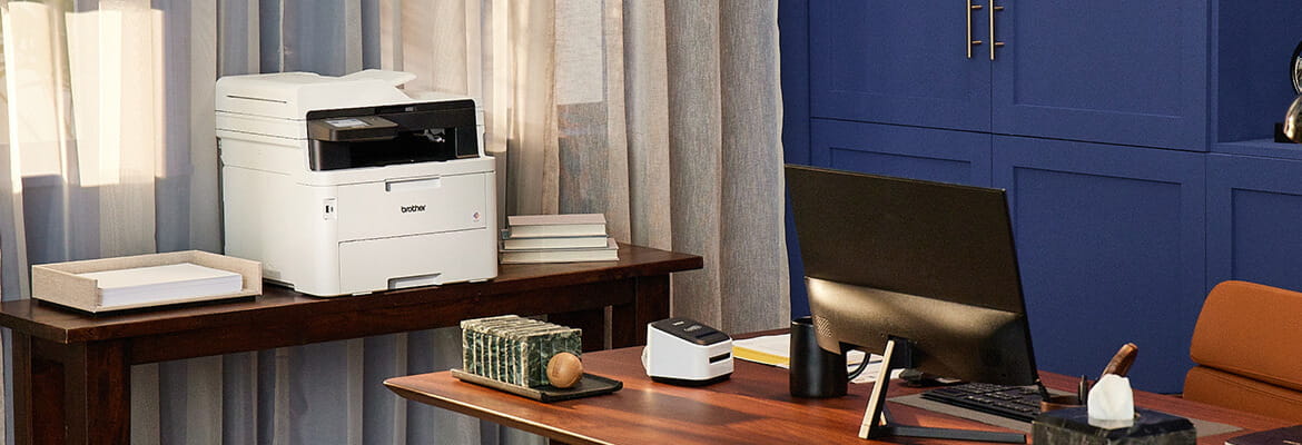 Brother printer in a home office setting with a QL label printer on the desk next to computer