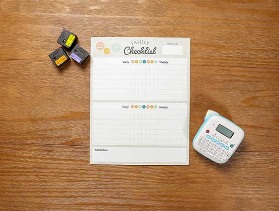 Blank chore chart on table next to Ptouch Btag label maker and various label tapes. 