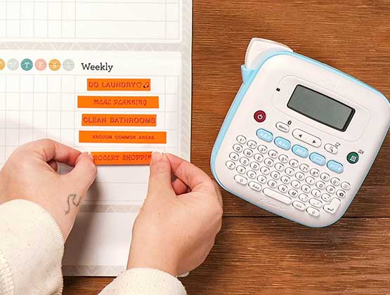 Person putting orange labels on the chore chart made with Ptouch Btag label maker. 