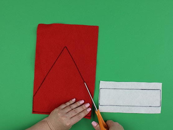 Person cutting red felt into triangle. Piece of white felt on the right with rectangle outline