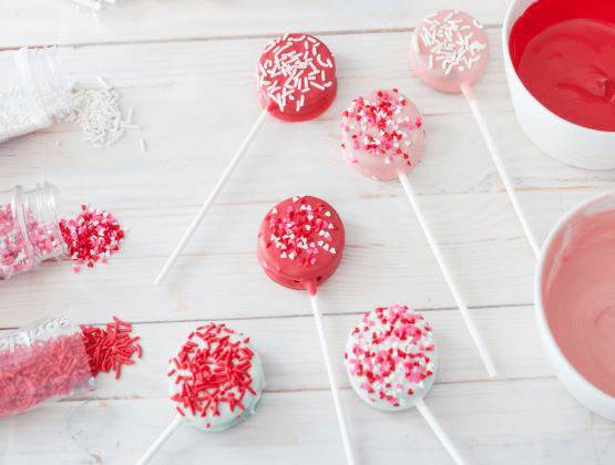 Decorated Oreo pops on a table with sprinkles and candy melts.