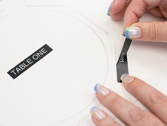 P-touch Embellish Craft Step 3 person putting label stickers around seating chart table.