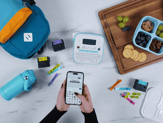 Brother Ptouch Label Maker with water bottles, label tapes, backpacks and food containers - Person with Phone typing in app in order to print