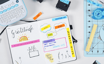 A white label maker surrounded by printed photos, scissors, and label tape on a crafting desk.