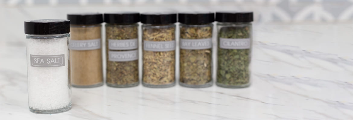 A variety of spices laying on marble countertop, with labels on them printed on brother ptouch