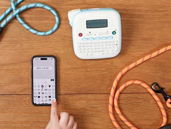 Person creating a label on a phone next to Btag label maker and leashes. 