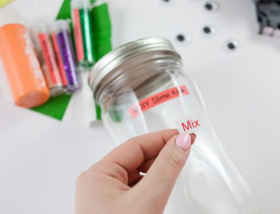 Person placing "Mix" label on a glass jar for DIY Slime kit
