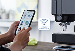 Mobile Phone with Artspira App Open standing next to Skitch Embroidery Machine for connecting with the machine