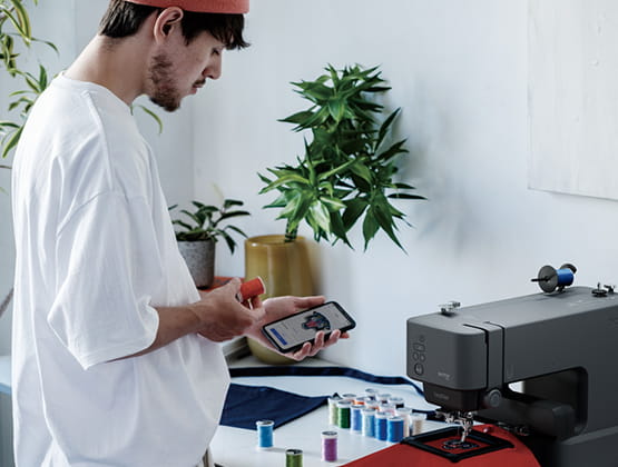 Person with phone standing next to Skitch Embroidery Machine while Skitch is embroidering