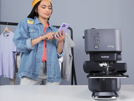 Girl Holding a phone with Sktich Embroidery Machine in front of her. 