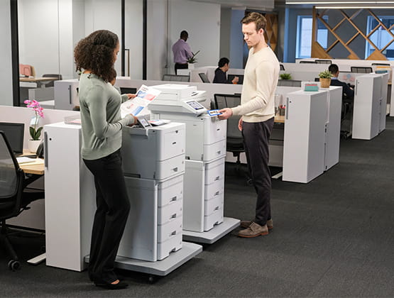 Two office employees utilizing printing and scanning capabilities on Brother enterprise printers and all-in-ones featuring HL-L9470 and MFC-L9670 models