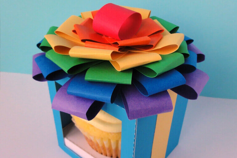 Cupcake in box with clear front, topped with multi-color ribbons to form a bow