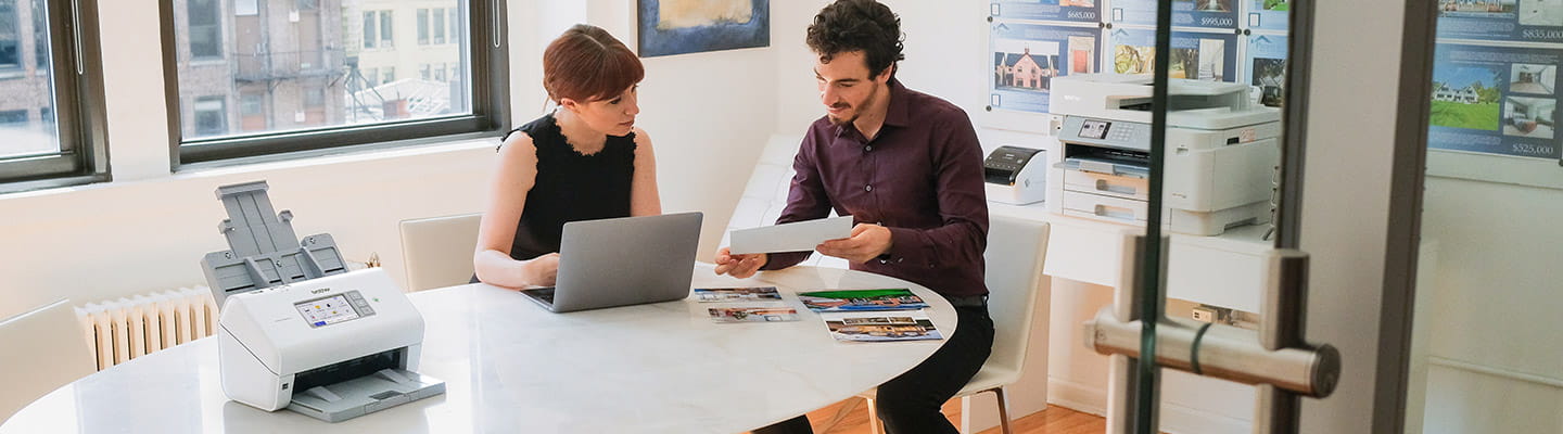 Man and woman collaborating on a project with ADS-4900W, QL-1110NWB, and MFC-J5955DW printers in office space.