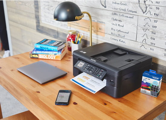 Brother printer on desk with phone and package of genuine Brother ink.