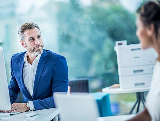 Man and woman talking at desks with HL-L9310CDW printer in background